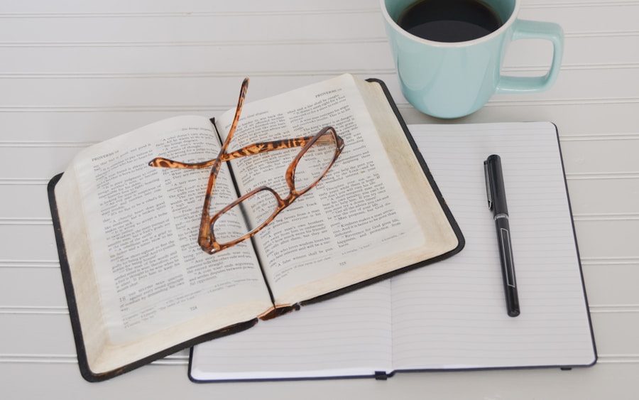 An open bible with glasses, a pen and a cup of coffee.