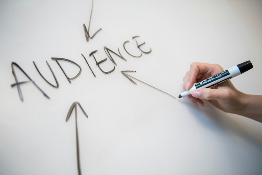 A person writing the word audience on a whiteboard.