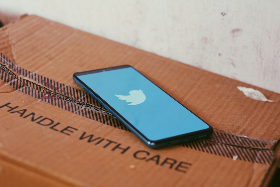 A cell phone with a twitter logo sitting on top of a cardboard box.