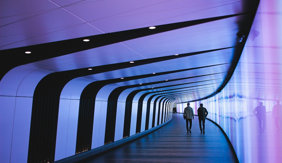 Two people walking down a tunnel with blue and purple lights.