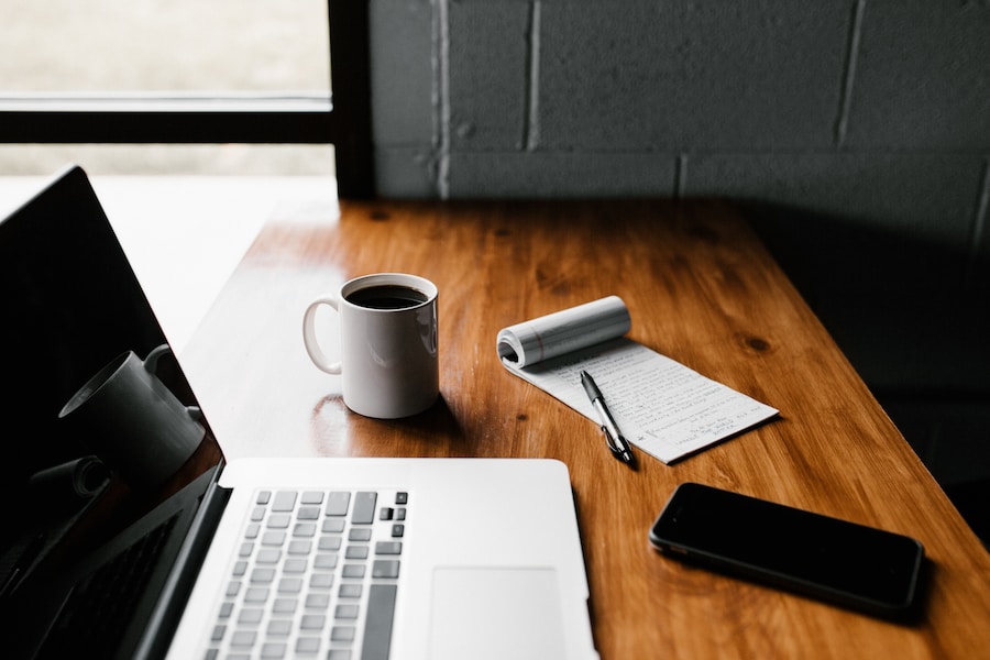 A laptop on a wooden desk with a cup of coffee.