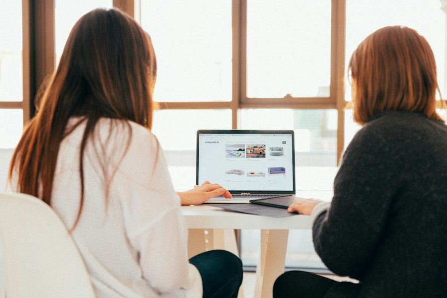 Two women sitting at a table looking at a laptop.