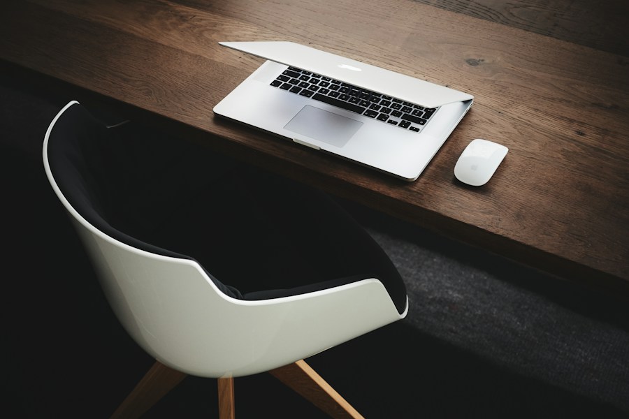 A white laptop on a wooden desk with a black chair.