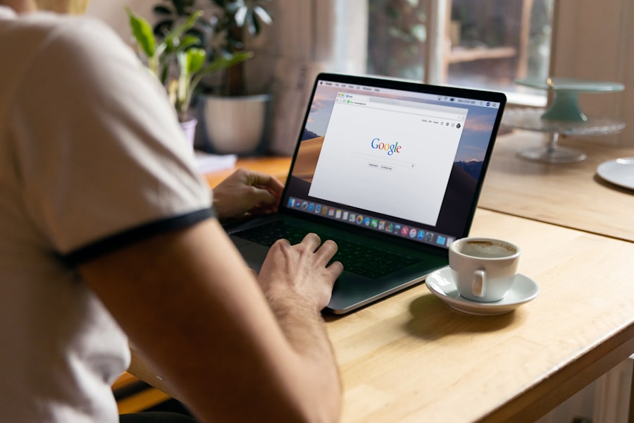 Person using a laptop displaying the google homepage at a wooden table with a cup of coffee beside it.