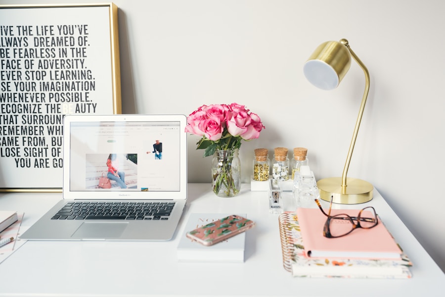 A modern workspace with a laptop, a desk lamp, a vase of pink roses, and various office supplies.