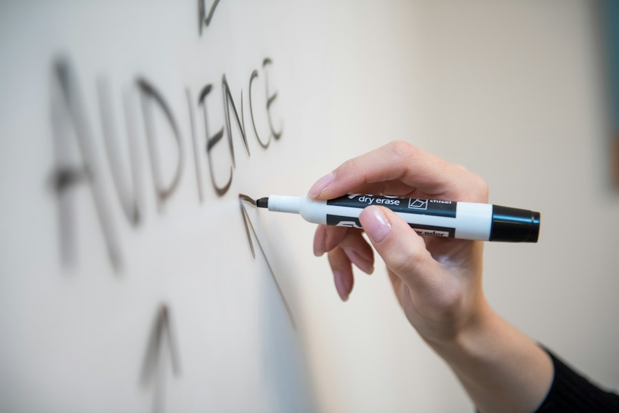 Close-up of a hand writing the word "audience" on a whiteboard with a black marker.