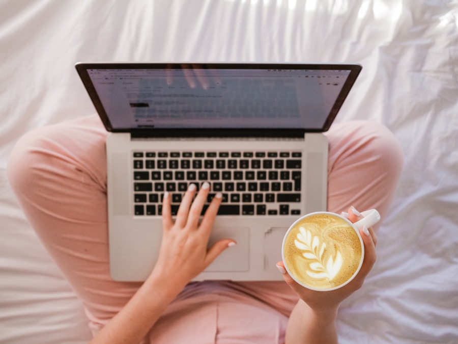 Person working on a laptop while holding a cup of coffee with latte art.