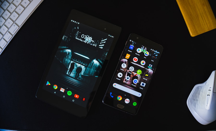 Two smartphones with different screens on display resting on a dark desk next to a computer keyboard and a white wireless earbud case.