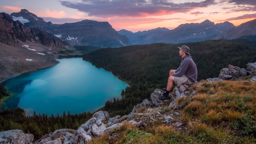 A person sitting on a rocky outcrop overlooking a serene alpine lake at sunset.