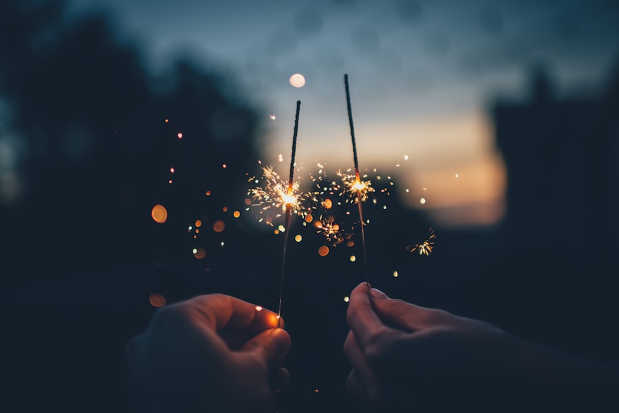 Two hands holding sparklers against a twilight sky.