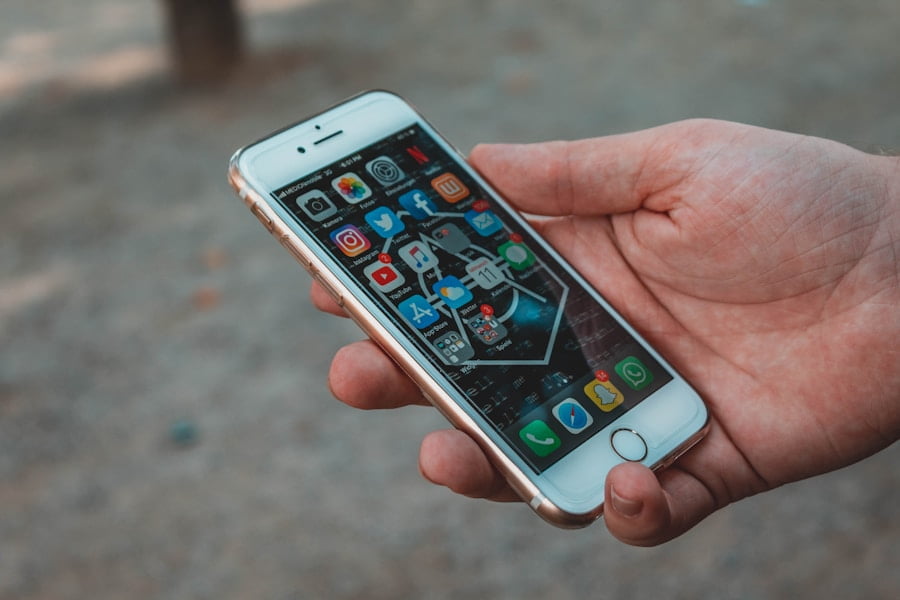 A hand holding a white iPhone displaying its home screen filled with various app icons.