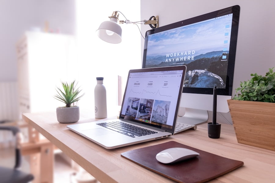 A desk with a laptop, monitor, mouse, lamp, plant, water bottle, and a graphics tablet. The monitor displays "WORK HARD ANYWHERE" above a scenic wallpaper.