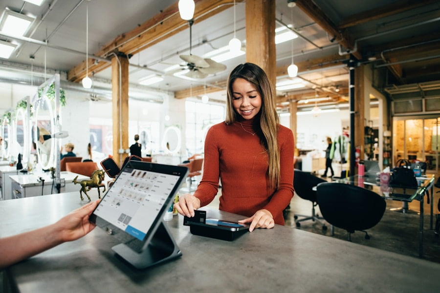 A woman in a red shirt uses a credit card reader at a counter in a bright, modern shop with wooden beams.