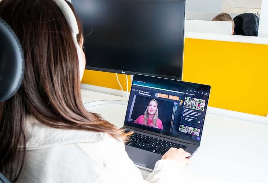 A woman uses a laptop in an office, participating in a video conference with another woman displayed on the laptop screen.