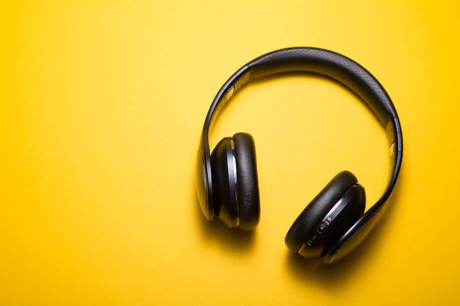 A pair of black over-ear headphones resting against a bright yellow background.