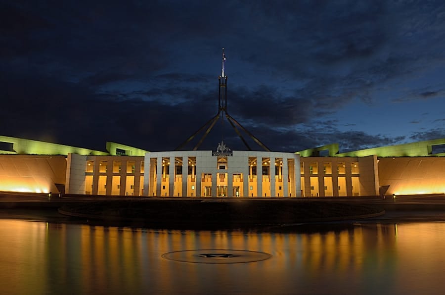 Parliament House in Canberra illuminated at night, with its iconic flagmast against a dark, cloudy sky.